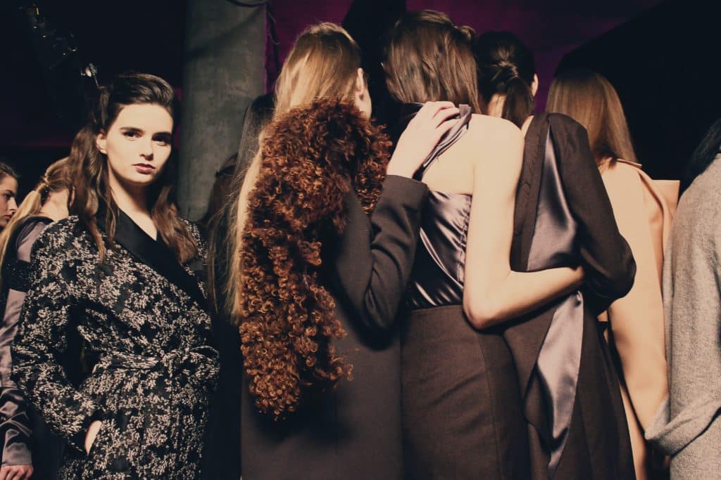 un groupe d’individus, probablement des mannequins, debout et proches les uns des autres. Ils portent divers styles de vêtements qui suggèrent un événement lié à la mode.